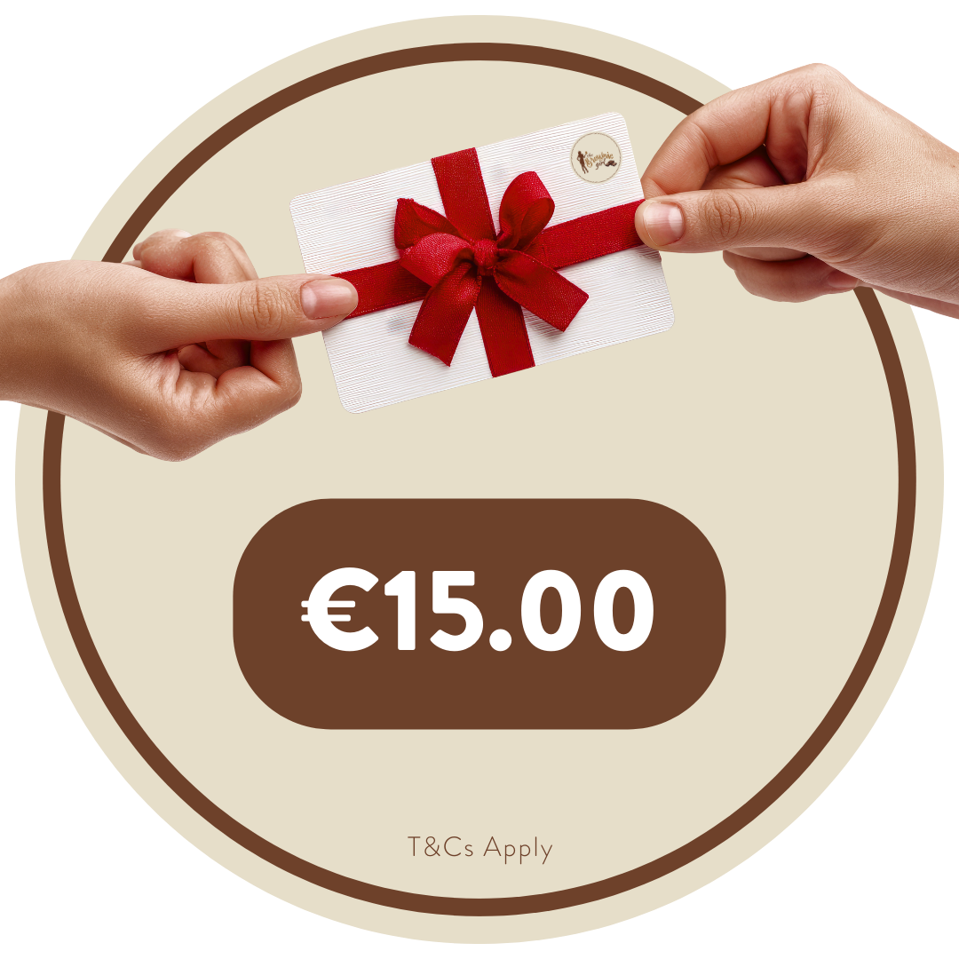 A €15 Brownie Girl gift card held between two hands, featuring a red ribbon and bow. The Brownie Girl logo appears in the top right corner of the card. The background shows soft beige and brown circular patterns, with “€15.00” displayed below the card and the note “T&Cs Apply” at the bottom