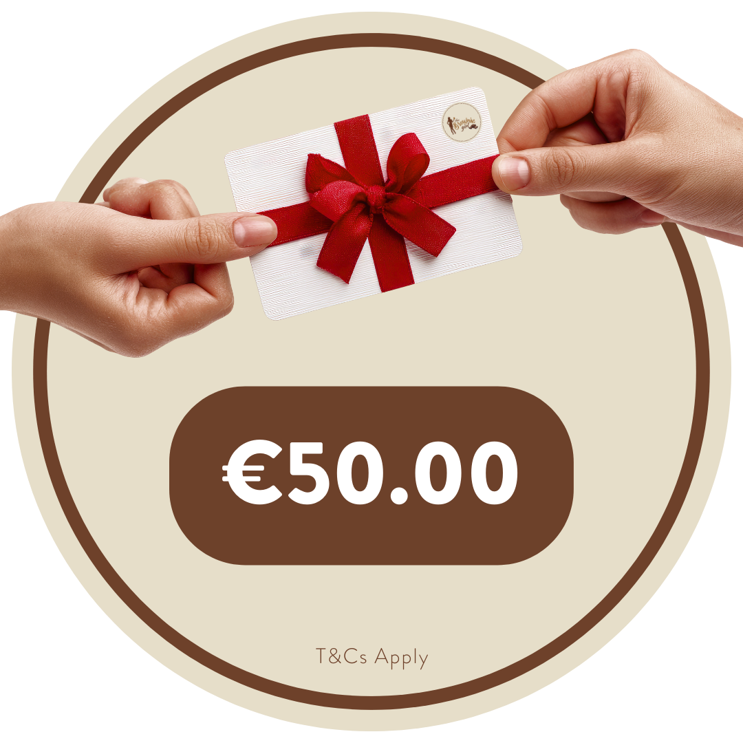 A €50 Brownie Girl gift card held between two hands, featuring a red ribbon and bow. The Brownie Girl logo appears in the top right corner of the card. The background shows soft beige and brown circular patterns, with “€50.00” displayed below the card and the note “T&Cs Apply” at the bottom