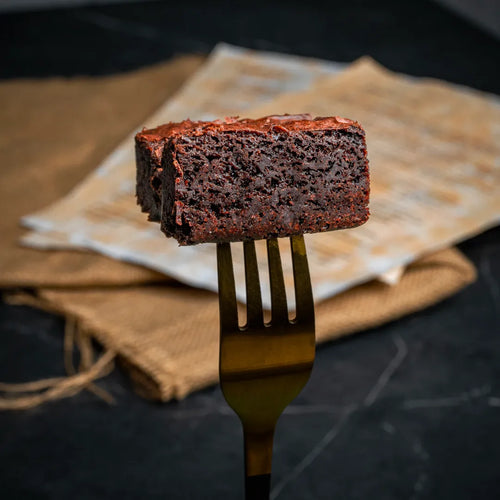 Close-up of a Classic Charm fudgy chocolate brownie held on a fork, showing its moist interior and glossy top, styled on a rustic background for artisanal dessert photography.