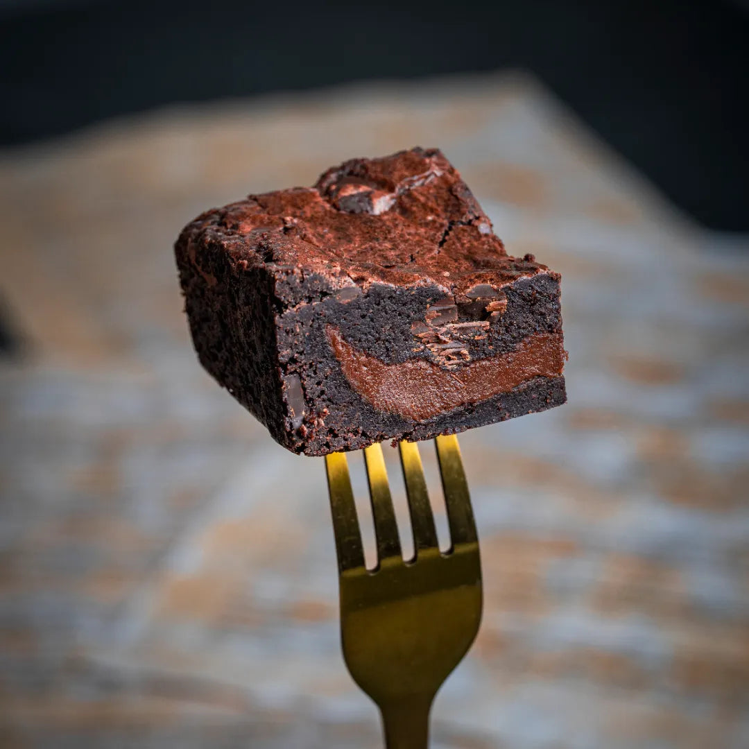 Close-up of a Delight with Pan Di Stelle Spread brownie held on a golden fork, showcasing its fudgy texture, melted chocolate swirls, and rich, indulgent interior.