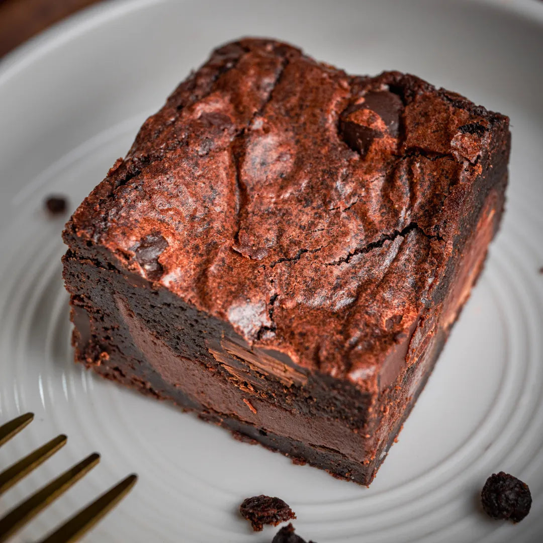 Single Delight with Pan Di Stelle Spread brownie on a white plate, highlighting its dense fudgy centre, chocolate chunks, and slightly cracked top crust.