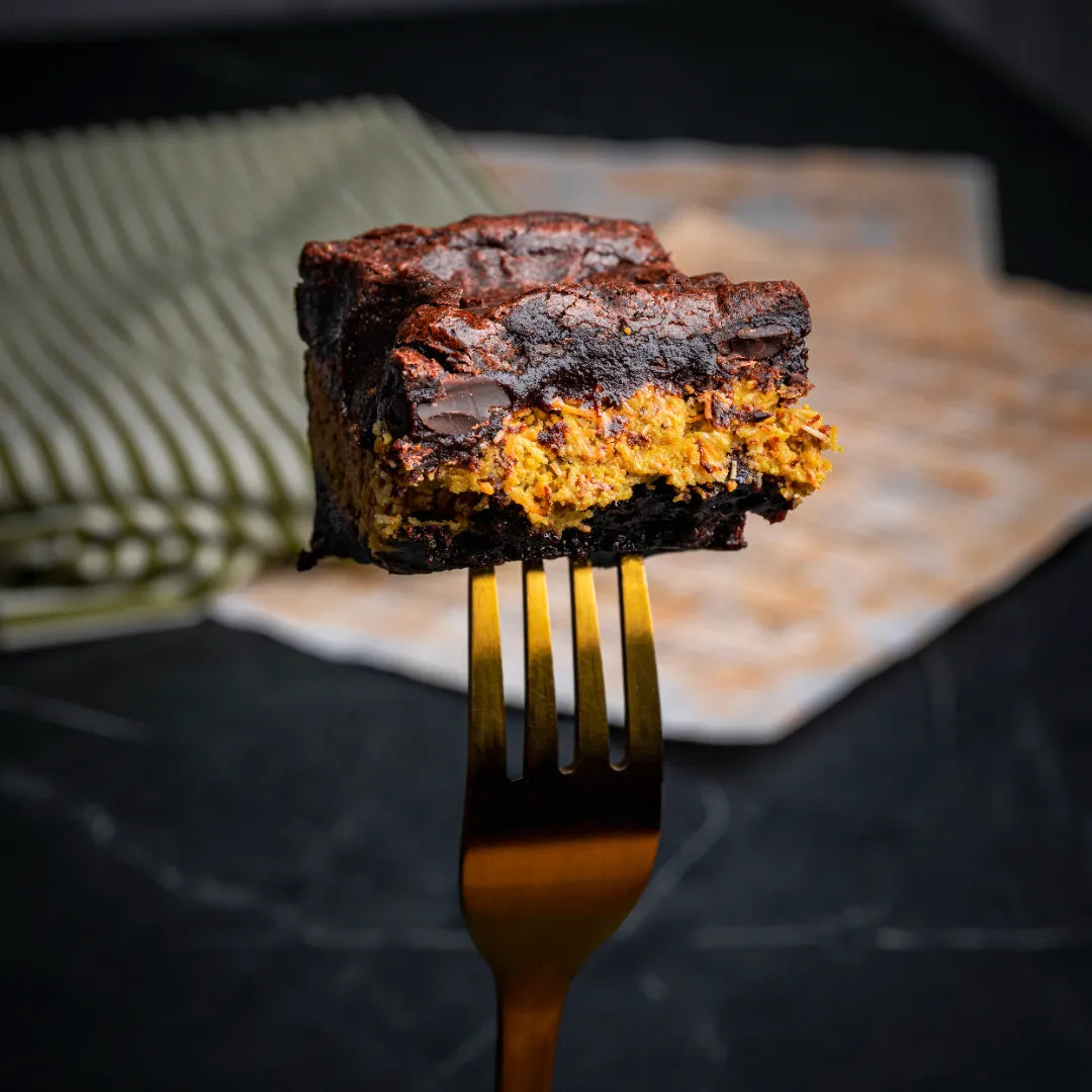 Close-up of a Dubai Brownie held on a golden fork, featuring a rich chocolate base with a vibrant kataifi and pistachio filling and a dense, fudgy texture.