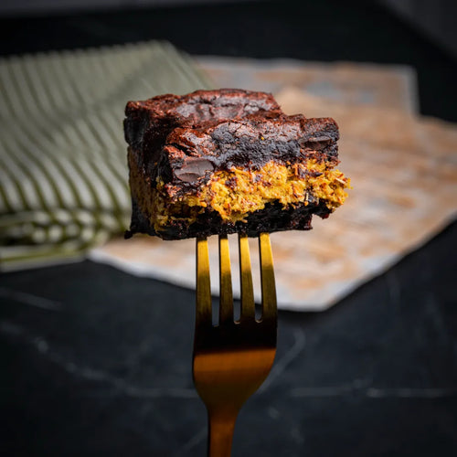 Close-up of a Dubai Brownie held on a golden fork, featuring a rich chocolate base with a vibrant kataifi and pistachio filling and a dense, fudgy texture.