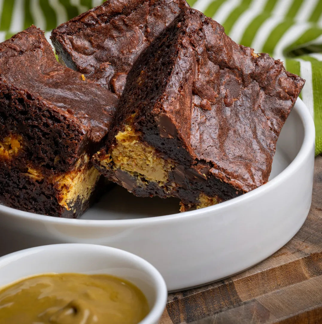 White bowl filled with three Dubai Brownies, highlighting their fudgy chocolate texture and bold pistachio and kataifi filling, served beside a dish of creamy spread.