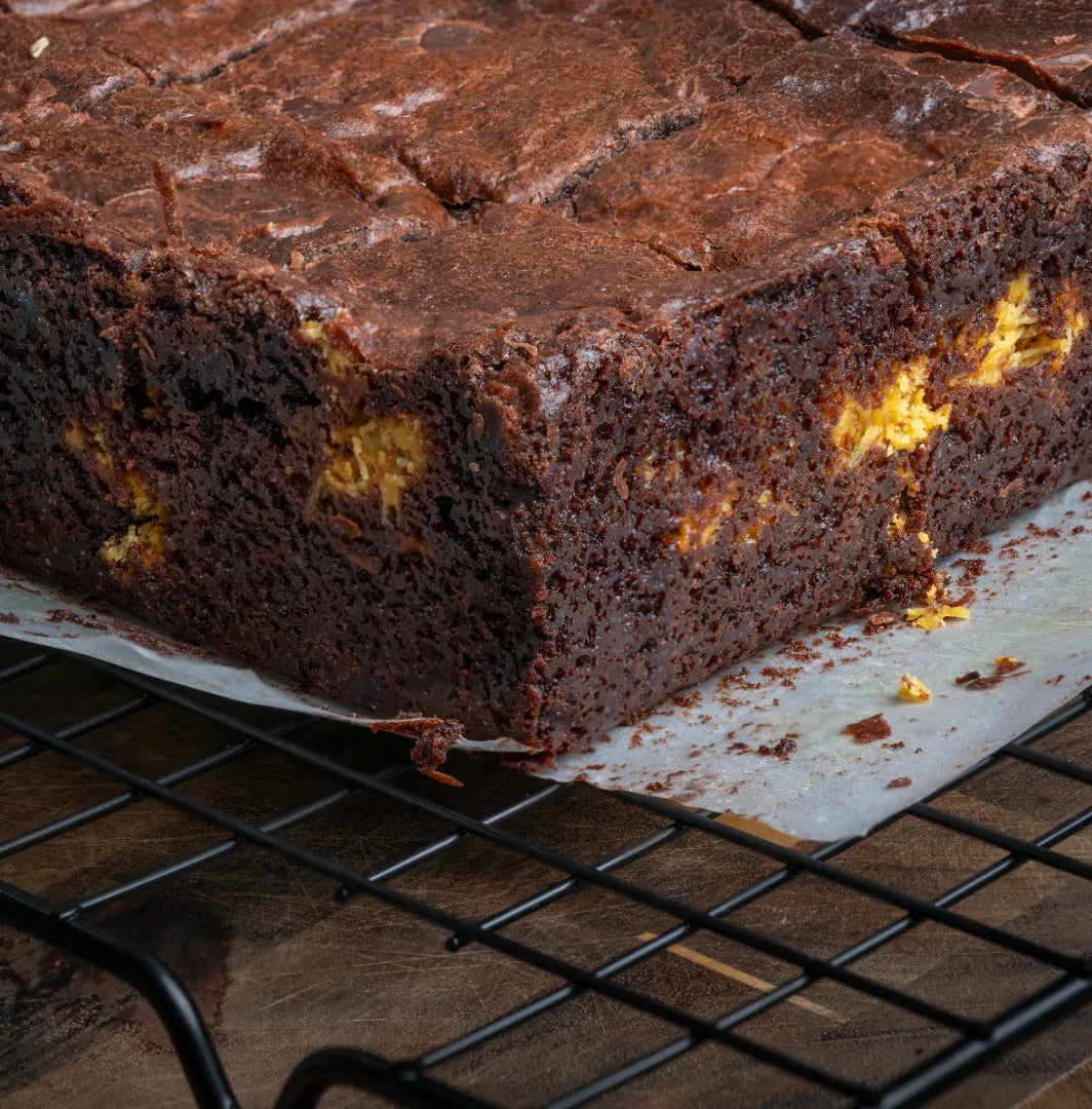 Freshly baked Dubai Brownies on parchment paper, showcasing their glossy chocolate top and swirls of bright kataifi and pistachio filling for a striking, indulgent look.
