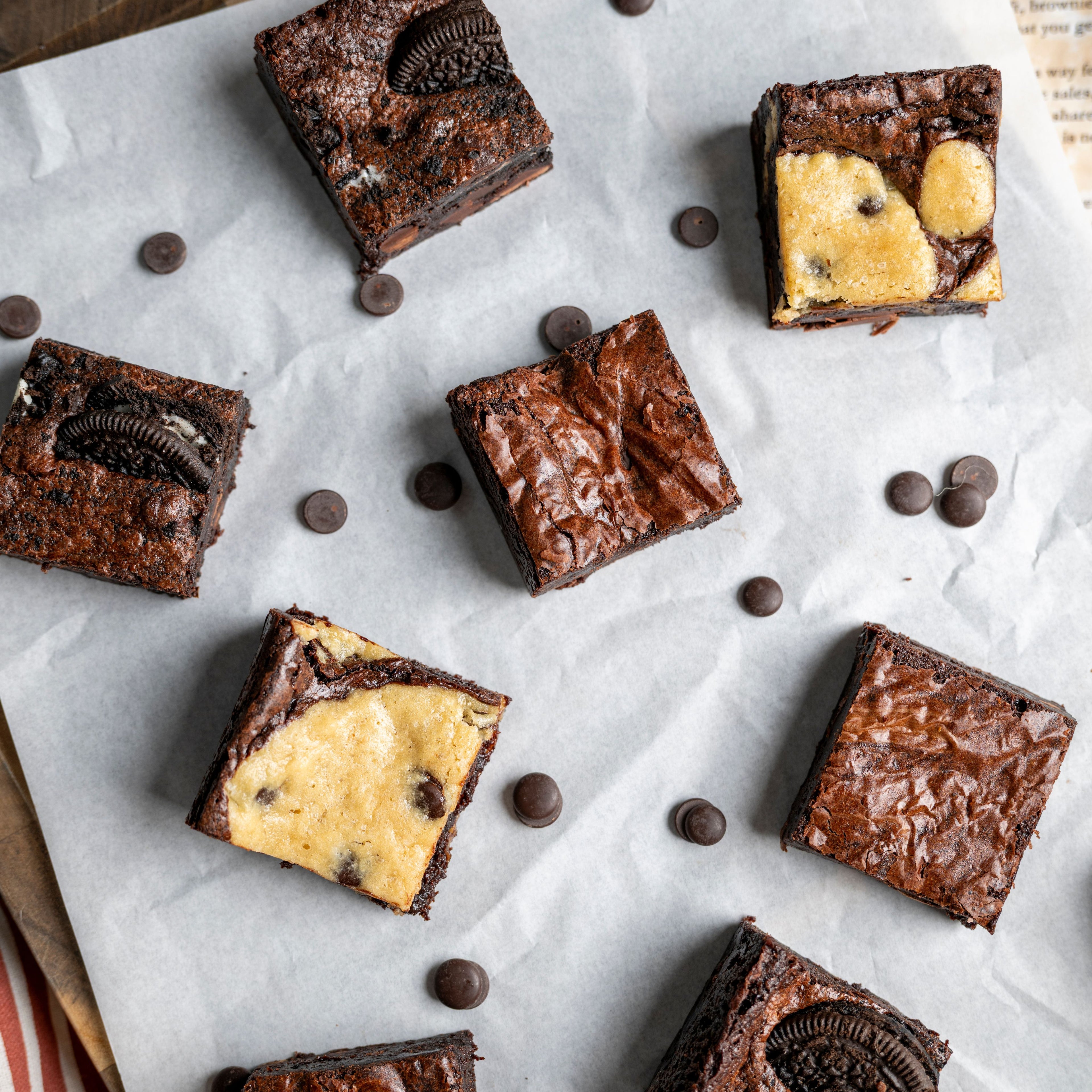 Rich chocolate brownies arranged on a wooden tray, featuring Oreo pieces, cookie‑dough swirls, and scattered chocolate chips.