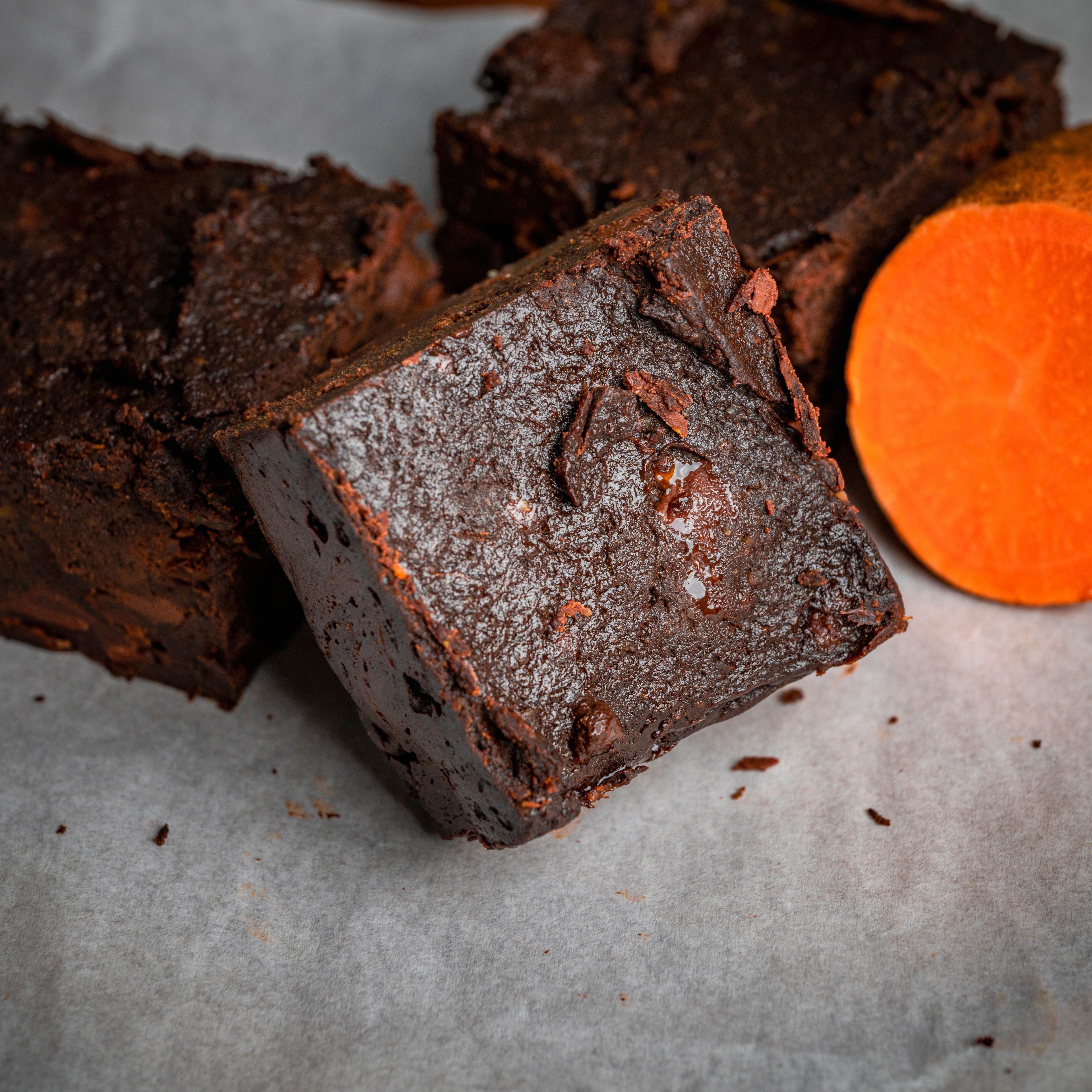 Close‑up of a fudgy chocolate brownie with visible chocolate chunks, styled beside a halved sweet potato to highlight sweet‑potato brownie ingredients.