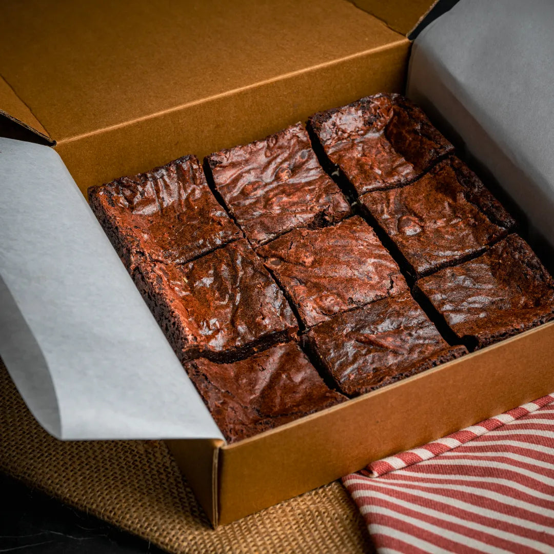 Box of nine Nuttelluxe brownies arranged in a grid, showcasing their glossy cracked tops and rich chocolate texture, packaged for gifting or bakery display.