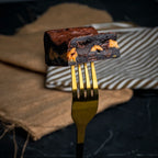 Close-up of a Nutty Buddy brownie held on a golden fork, showing its fudgy chocolate texture and thick Reese’s peanut butter layer.