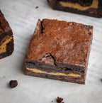 Close-up of a Nutty Buddy brownie with a rich chocolate exterior and creamy Reese’s peanut butter filling, surrounded by additional brownie pieces.