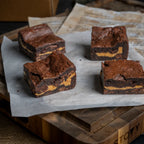Four Nutty Buddy brownies on parchment paper, each with a fudgy chocolate top and a thick Reese’s peanut butter layer in the centre.