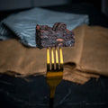 Close-up of an Oreo Dreams brownie held on a golden fork, showing its fudgy chocolate texture and chunks of crushed Oreo biscuits throughout.