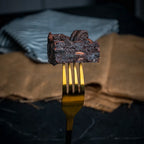 Close-up of an Oreo Dreams brownie held on a golden fork, showing its fudgy chocolate texture and chunks of crushed Oreo biscuits throughout.