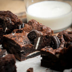 Rich Oreo Dreams brownies with crushed Oreo biscuits baked inside, served beside a glass of milk for a classic cookies‑and‑cream dessert moment.